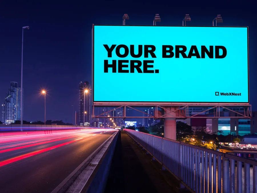 A digital billboard over a freeway at night reading Your Brand Here.