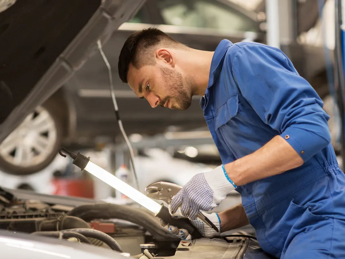 A mechanic working under the hood of a car in a garage.