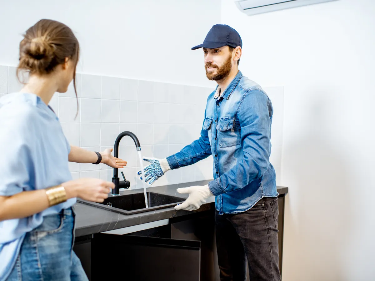 A plumber talking with a homeowner at her kitchen sink.