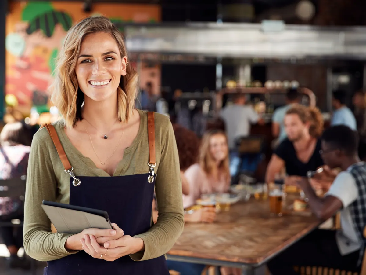 A server holding menus in a busy restaurant.