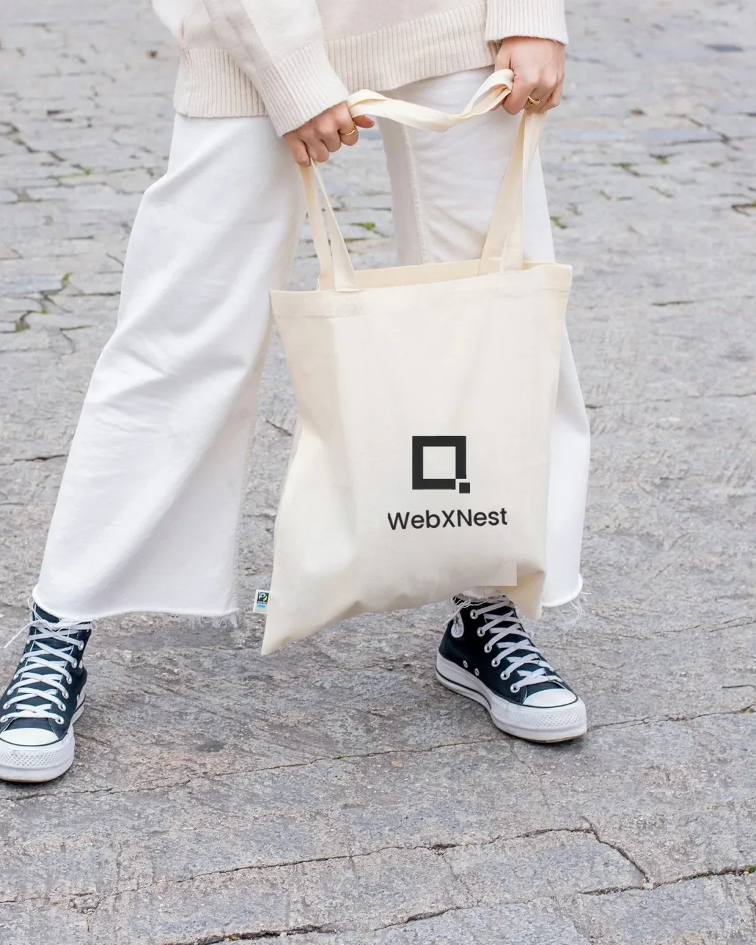 A canvas tote bag printed with the WebXNest logo, carried on the street.