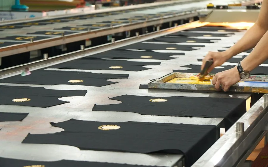 Black shirts on a screen-printing line, a printer pulling ink across a screen.