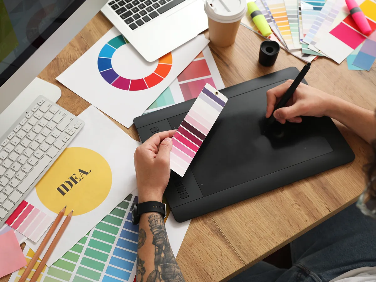 A designer sketching on a tablet among color swatches and brand ideas.