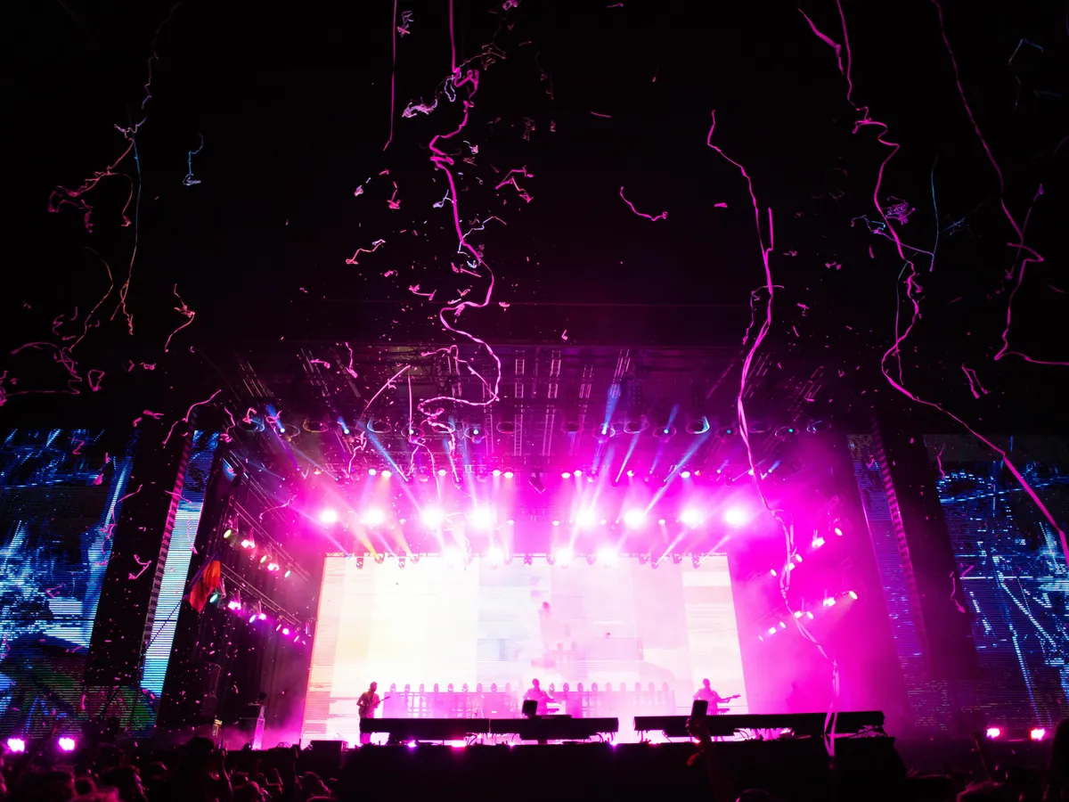 A concert stage lit up in pink, with streamers in the air.