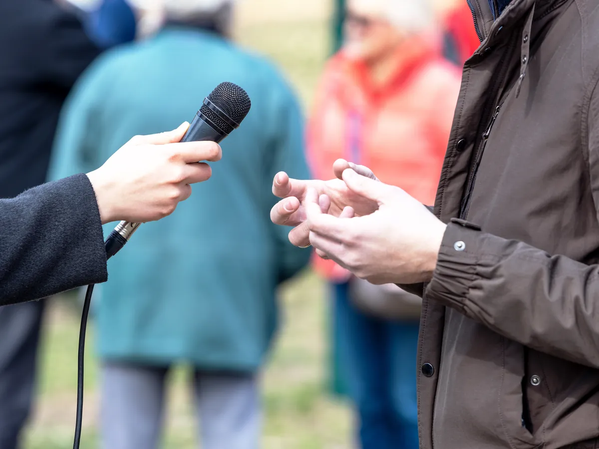 A reporter holding out a microphone to a man being interviewed outdoors.