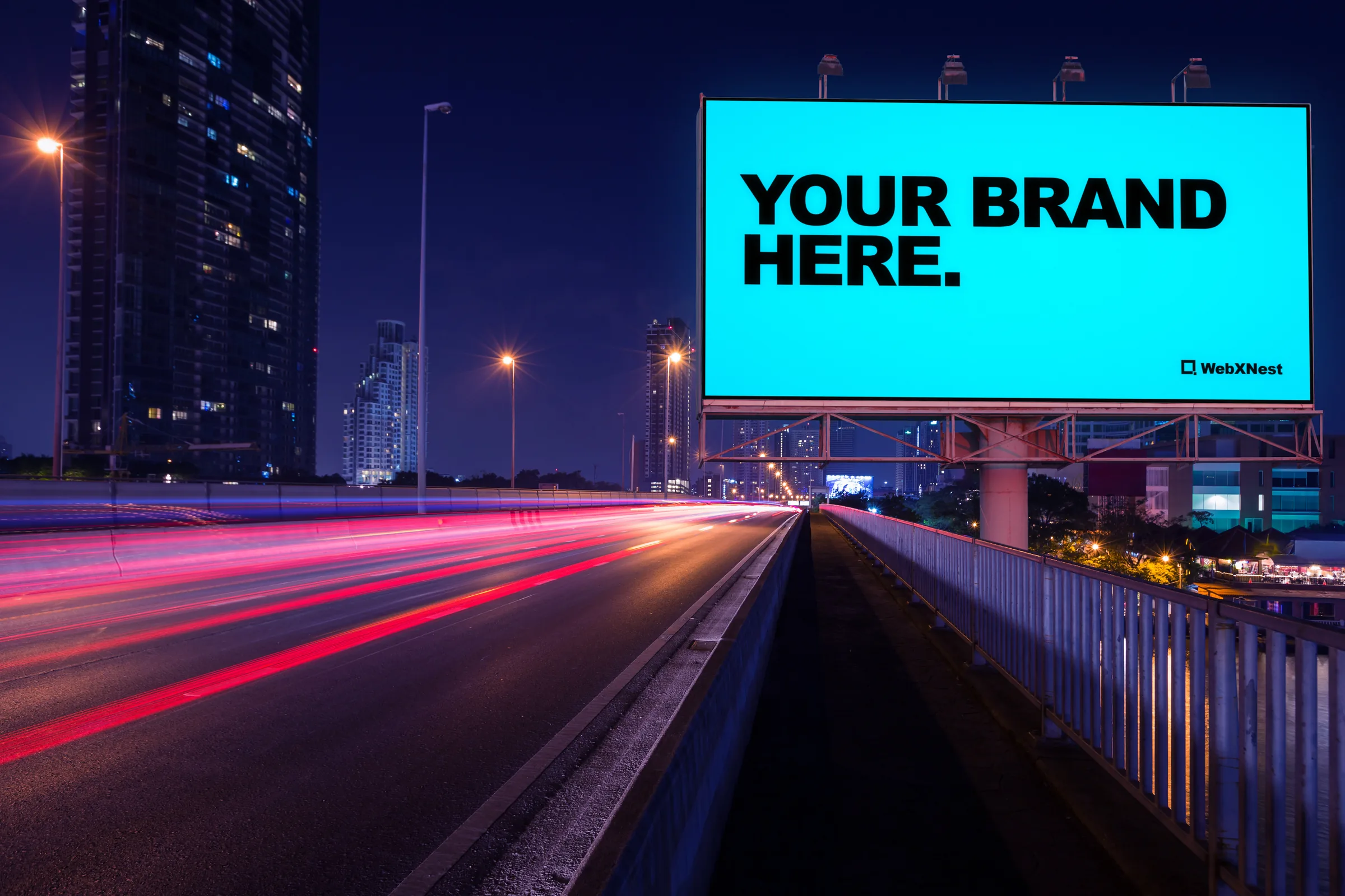 A digital billboard over a highway at night, its screen reading &ldquo;Your brand here.&rdquo;