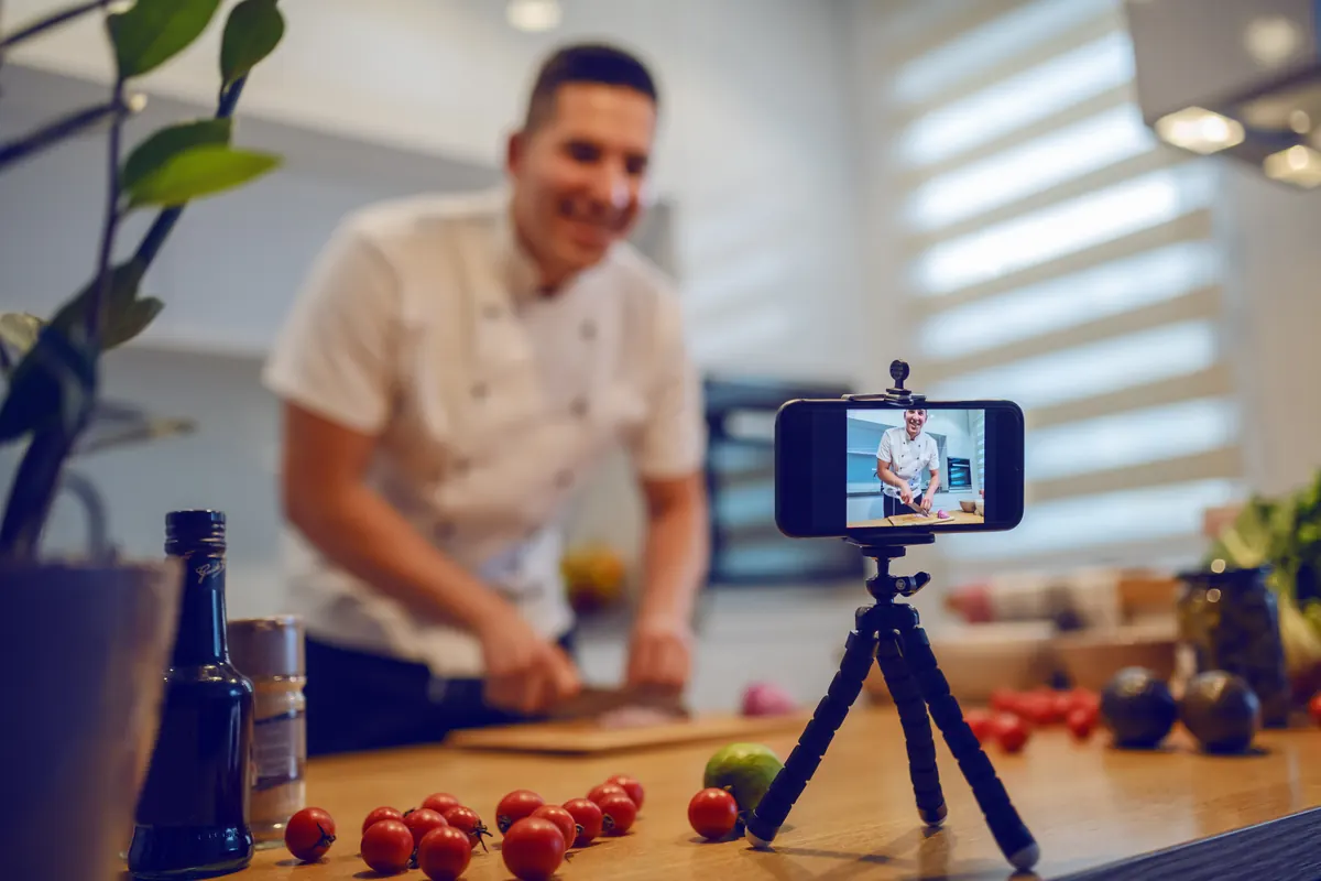 A chef filming himself cooking on a phone on a small tripod.