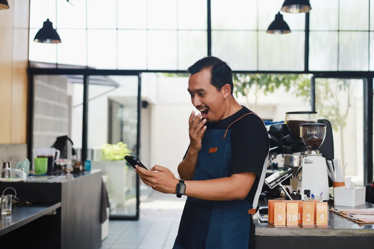 A caf&eacute; owner reacting to good news on his phone.